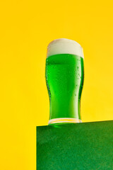 Festival drink. Glass of foamy frothy green beer over bright yellow background. Traditional taste....