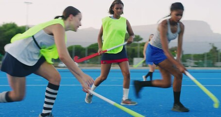 Diverse team of young field hockey players playing on astroturf in a game. Young girls practicing at school. Full length mixed race female dribbling the ball with her hockey stick - Powered by Adobe