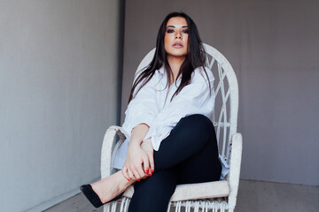 a brunette woman in a white beauty shirt sits on a chair