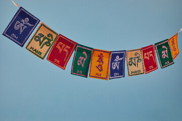 Tibetan Buddhist flags against blue background. Text on flags Om mani padme hum meaning The jewel is in the lotus. - obrazy, fototapety, plakaty
