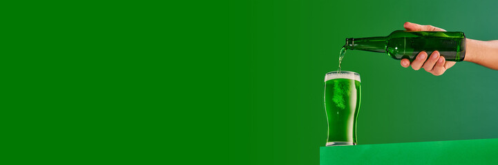 Male hand pouring green foamy frosty beer into glass over green background. Concept of st patrick's...