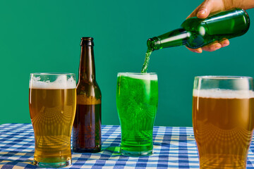 Bottle and glasses with lager and green foamy beer on checkered tablecloth over green background. Concept of st patrick's day celebration, brewery, traditions, alcohol drinks, taste, Irish holiday