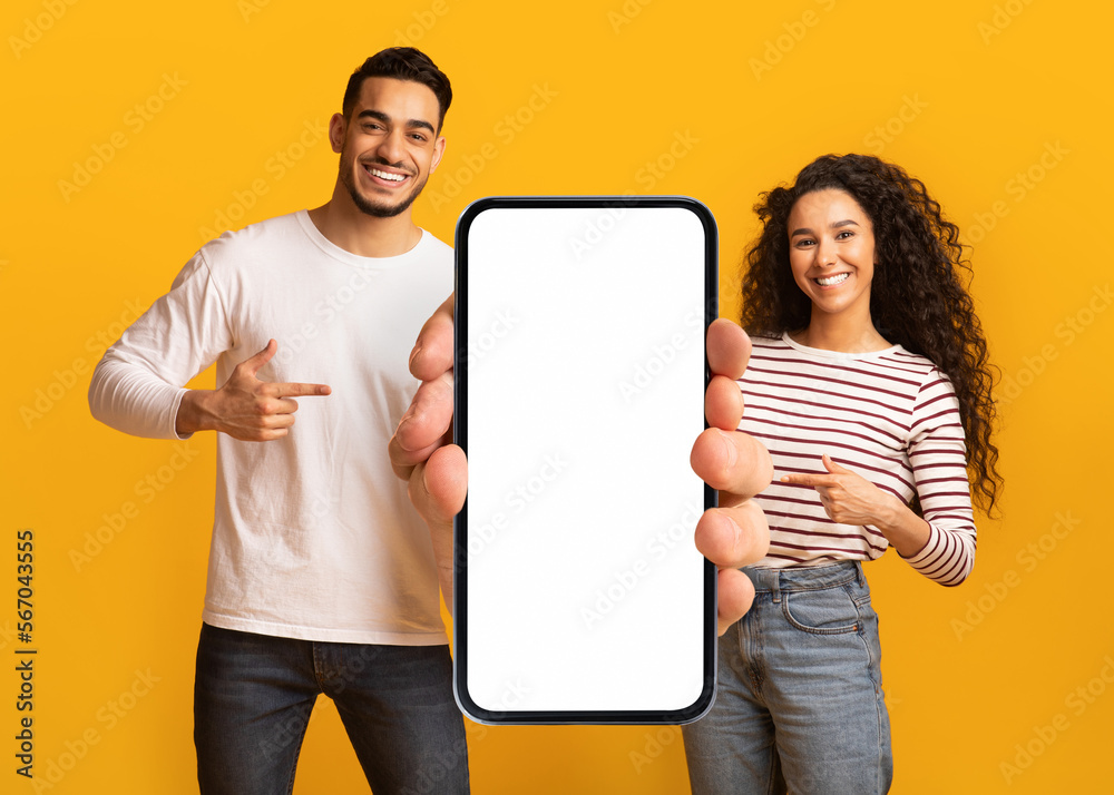 Wall mural nice offer. smiling middle eastern couple pointing at big blank smartphone