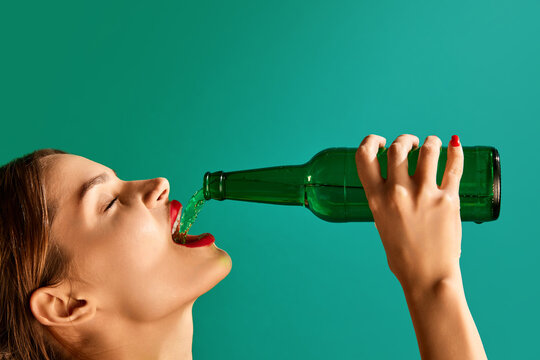 Woman pouring green beer into her mouth over green studio background. Concept of st patrick's day celebration, brewery, traditions, alcohol drinks, taste, Irish holiday - Powered by Adobe