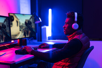 Young African man playing video game on computer. Streamer guy sitting at home and plays another match..