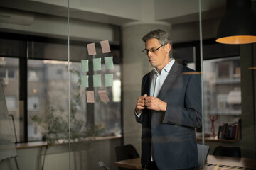 Portrait of successful businessman in office. Man writing ideas on colorful stickers on glass wall.
