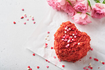 Two cakes Red velvet in shape of hearts on white plate, rose flowers and cup of coffeeon on pink romantic background. Dessert idea for Valentines Day, Mothers or Womens Day. Tasty homemade dessert.