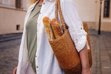 Woman with baguette bread in straw bag. Sustainable lifestyle and reusable shopping bag