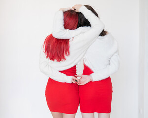 Rear view of two women dressed in identical red dresses and white sweaters. Lesbian intimacy. White background.