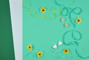  Birthday or Valentines day greeting mockup with frame from wavy yellow- green  ribbons and decorations : yellow decorative flowers, hearts and rattan balls on green mint background .Top view flat lay