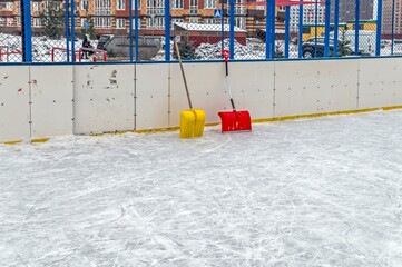 A red and yellow shovel stands against the wall of the hockey field