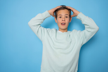 Young emotional handsome boy standing on blue studio background. Human emotions, facial expression concept.