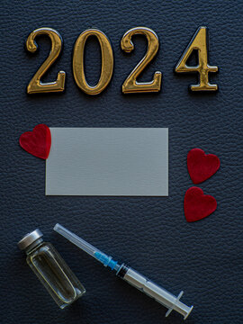 2024, medicine and Vaccination concept. Close up view photo of 2024 and place for text on dark background. Christmas medical card with paper red hearts, syringe, vaccine bottle and copy space. 