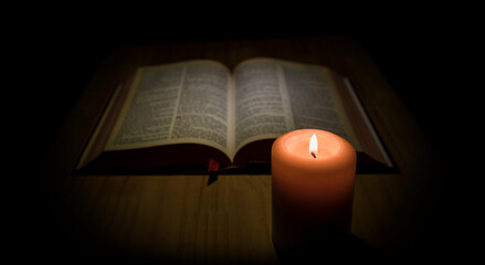 Fototapeta na wymiar A holy bible and candle on the table. Bible illuminated by a light and a lit candle in the dark. 