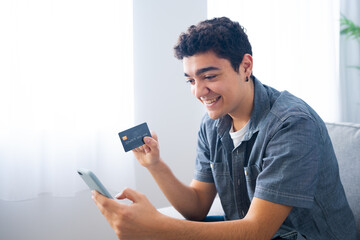 Hispanic teenager boy shopping online on phone, holding credit card