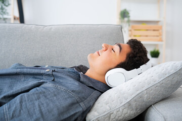 Fototapeta premium Hispanic teenager boy listening relaxing music on headphones while lying on back on sofa
