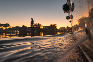 sunset on the water reflecting on the yacht with trees in silhouette,  