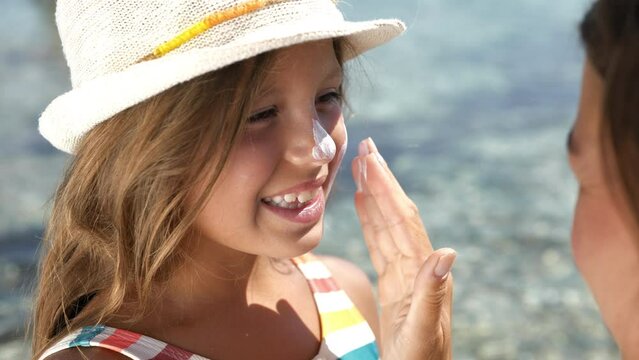 Portrait of a Little Girl Laughing and Smiling While her Mother Puts Sunscreen on her Face During Their Visit to the Beach. Young Woman Protecting her Daughter's Skin From Sun During Summer Vacation