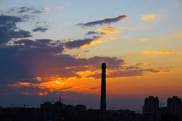 Fototapeta na wymiar Outline of tall chimney tower and buildings during sunset with dramatic clouds and colors.