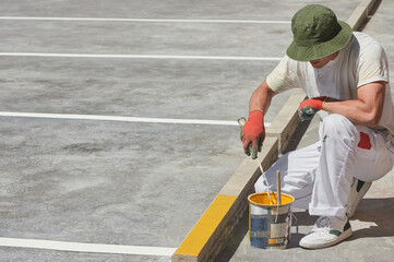 Professional painter at work. Young man uses a paint roller to apply special acrylic paint for road marking on asphalt of a parking lot.