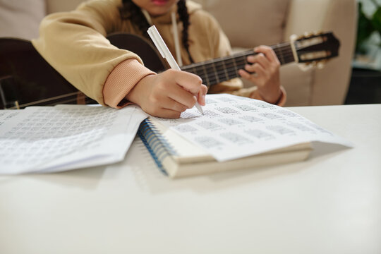 Girl taking notes in textbook when playing guitar at home