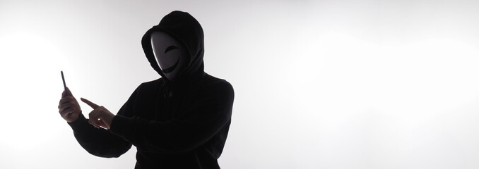 Hacker Anonymous and face mask with smartphone in hand. Man in black hood shirt holding and using...