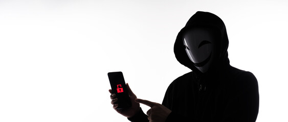 Hacker Anonymous and face mask with smartphone in hand. Man in black hood shirt holding and using...