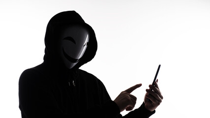 Hacker Anonymous and face mask with smartphone in hand. Man in black hood shirt holding and using...