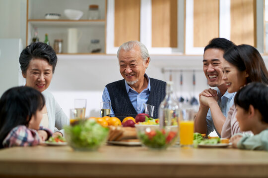 three generation happy asian family chatting while eating meal