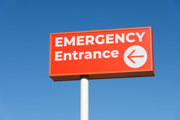 Emergency Entrance sign in red and white isolated against blue sky with arrow