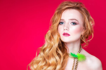 A beautiful choker made of gold chains and green fluff around the neck of a red-haired girl. Woman posing on red background in studio