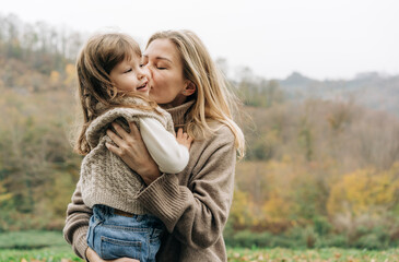 Mom kisses a little charming daughter, holding in her arms.