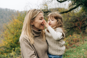 Fototapeta premium A little daughter in her mother's arms grimaces and fools around with her mother's nose.