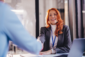 a young woman smiling and shaking hands with a client, after concluding a contract