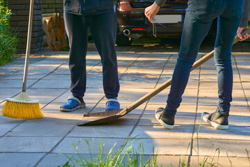 Legs of a man and a woman cleaning the house yard with a shovel and a broom