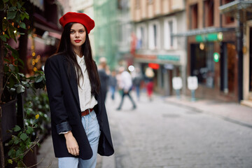 Fototapeta premium Woman fashion model stands on the street in the city among the crowd in a jacket and red beret and jeans, cinematic french fashion style clothing, travel to istanbul