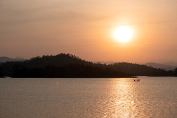 Naklejka premium Beautiful sunset behind the mountain silhouette in Kaeng Krachan Reservoir, located in central of Thailand, boat drives in a reservoir far away