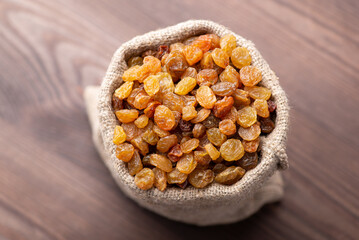 Raisin in linen sack on wooden table. Close up of fresh tasty raisin in small cloth bag on wooden background