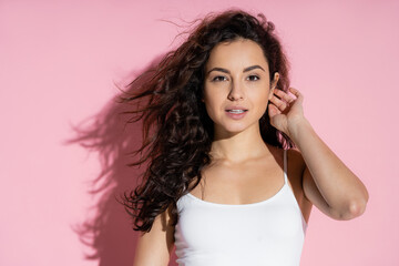 Naklejka premium Portrait of young curly woman looking at camera on pink background.