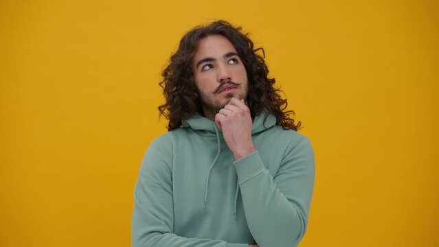 Pensive long-haired man in a blue hoodie thinking about something in the yellow studio