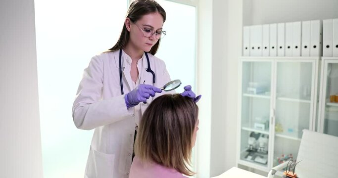 Ttrichologist doctor examines patient scalp through magnifying glass in clinic