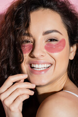 Portrait of curly young woman with eye patches looking at camera on pink background.