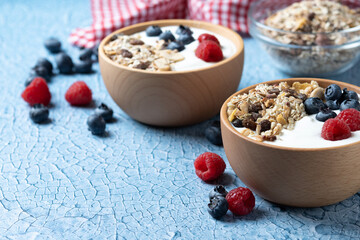 Yogurt with berries and muesli for breakfast in bowl on bue background. Copy space