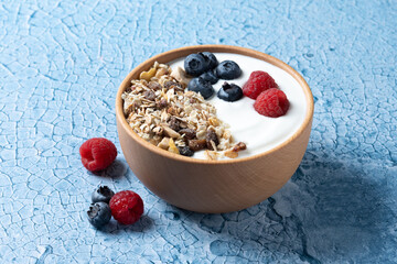 Yogurt with berries and muesli for breakfast in bowl on bue background