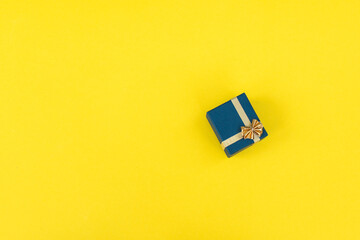 A small gift box with a gold ribbon and a bow on a yellow background