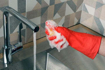 young woman washes dishes. a girl in red gloves washes dishes with a yellow sponge.