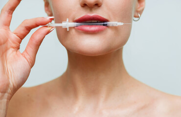 Closeup face young woman holds syringe in mouth. Hyaluronic acid collagen injection for lips