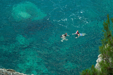 Two girls in snorkeling masks swim in the turquoise sea water near the shore. Aerial top view of snorkeling. Travel, water sports. Active recreation, outdoor adventure. Selective focus. Copy space