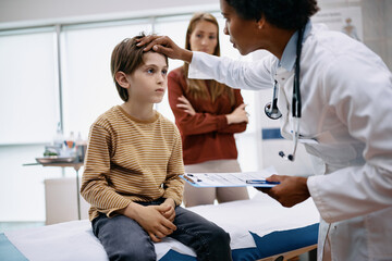 Obraz premium African American pediatrician examining small boy during medical appointment at doctor's office.
