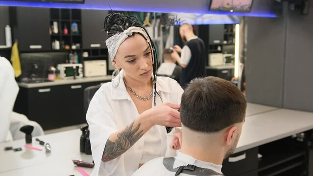 A stylish female hairdresser cuts the hair of a man in a barber shop